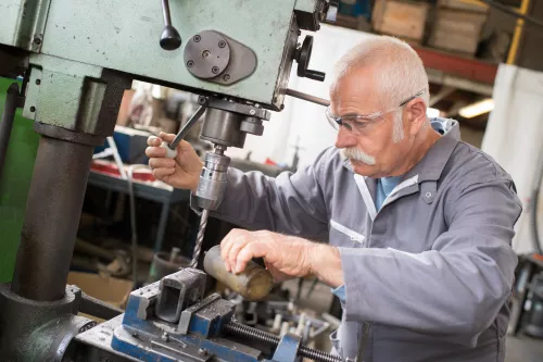 senior metal worker using industrial drilling machine in workshop