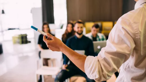 Formateur sur la droite se tenant debout, et de dos, devant quelques personnes attentives